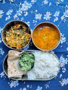 three metal containers filled with food on top of a blue floral tablecloth covered ground