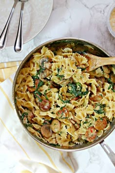 a pan filled with pasta and vegetables on top of a table next to utensils