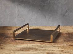 a square metal tray sitting on top of a wooden table next to a gray wall