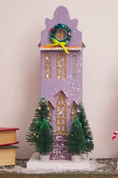 a purple clock tower sitting on top of a table next to books and christmas decorations