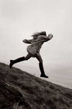 a woman jumping up into the air on top of a grass covered hill in black and white