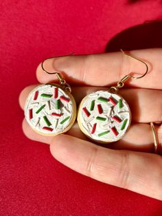 a pair of earrings that are in someone's hand with red and green sprinkles on them