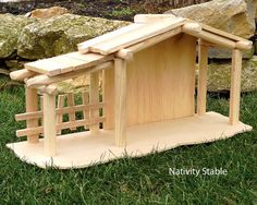 a small wooden structure sitting on top of some grass next to rocks and trees in the background