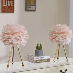 two pink lamps sitting on top of a white dresser next to a potted plant