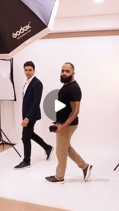 two men are walking in front of a photo studio and one is holding an umbrella