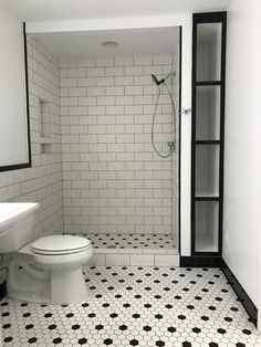 a white toilet sitting in a bathroom next to a walk in shower with black and white tile