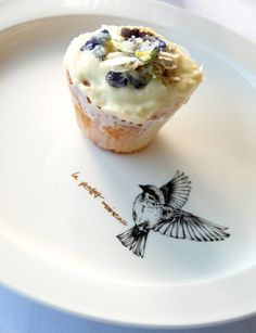 a cupcake with frosting and blueberries is on a plate next to a drawing of a bird