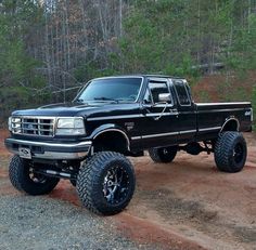 a black pickup truck parked on top of a dirt road next to trees and bushes