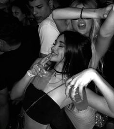 several people are dancing and having drinks at a club or bar, one woman is holding a wine glass up to her mouth