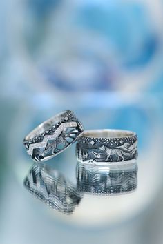 two wedding rings sitting next to each other on top of a reflective surface with blue and white swirls in the background