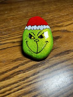 a green rock with a red santa hat on it's head and eyes drawn on it