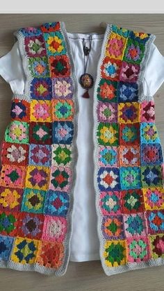 a colorful crocheted vest is hanging on a wooden table with a white t - shirt underneath it