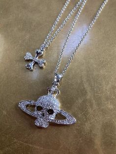 two necklaces that have been placed on top of each other, one with a skull and the other with a cross