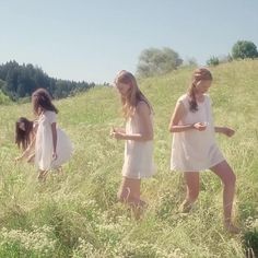 three girls in white dresses walking through tall grass