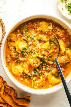 a white bowl filled with tortellini soup on top of a table next to bread