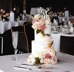 a white wedding cake with flowers on top and the word mr and mrs spelled in cursive