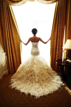 a woman standing in front of a window wearing a dress with feathers on the skirt