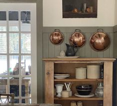 a wooden table topped with lots of bowls and pans next to a wall mounted painting