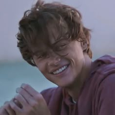 a young man with curly hair smiling and holding his hands together in front of him