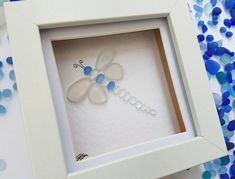 a white frame with blue and white flowers in it on a table next to confetti