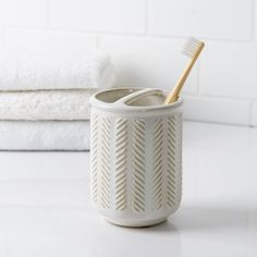 a toothbrush holder sitting on top of a white counter next to towels and folded towels