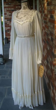 "This is a lovely, Romance Style Gunne Sax dress in a loosely woven, cream gauze, permanently pleated and running longitudinally with a dainty calico of violet flowers accenting the bodice and high waist (empire). There are gauze sashes on either side of the waist for adjustment.' The sleeves are unlined and billowing with a single button, calico cuff for whimsy. So much of it's beauty lies in its sumptuous skirting, simplicity and that 10 inch bottom ruffle living amongst ribbon and lace. Due t Gunne Sax Dress Vintage 70s, Light Cottagecore, Antique Dress Form, Vintage Gunne Sax Dress, Coquette Princess, Pleaded Skirt