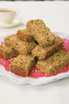 some oatmeal bars are on a red and white plate next to a cup