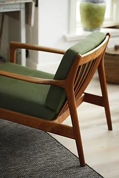 a green chair sitting on top of a wooden floor next to a table with a vase