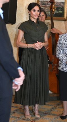 the woman is wearing a green dress and standing in front of two women with musical instruments