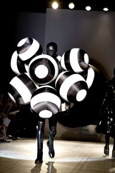 a woman walking down a runway with lots of black and white balls on her back