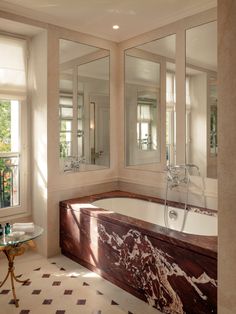 a bath tub sitting under three mirrors next to a table with a vase on it