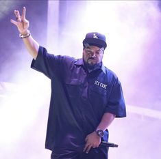 a man standing on top of a stage with his hand in the air and wearing a hat