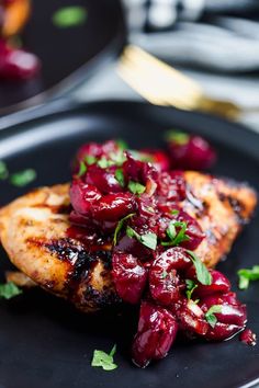 a black plate topped with meat covered in cherries