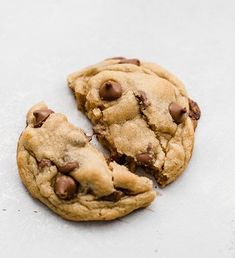 two chocolate chip cookies sitting on top of a white countertop next to each other