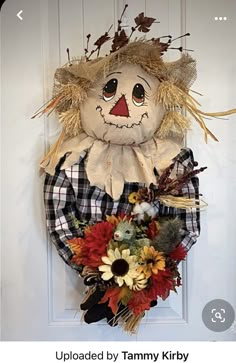 a scarecrow door hanger is decorated with flowers and hay for the fall season