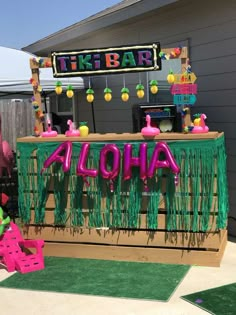 a tiki bar decorated with neon green grass and pink balloons that spell out the word aloha