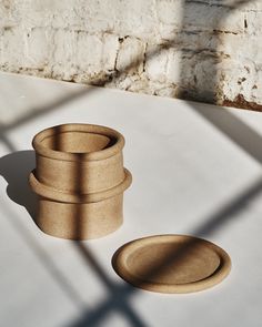 three wooden bowls sitting on top of a white table next to a brick wall and shadow