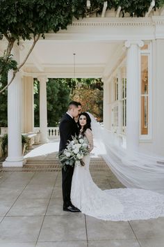 a bride and groom standing in front of a white building with columns on either side