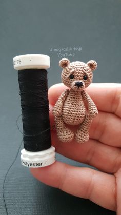 a tiny teddy bear sitting on top of a spool of thread next to a needle