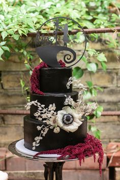 a three tiered black wedding cake with white flowers and an acrylic music note on top