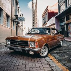 an old car is parked on the street in front of some buildings and brick pavement