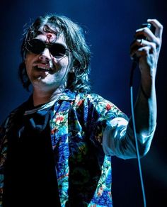 a man with long hair and sunglasses holding a microphone in his right hand while standing on stage