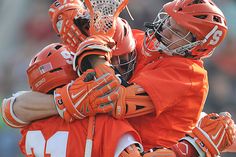 two lacrosse players hugging each other in an orange uniform on the field with fans watching