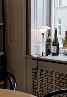 two bottles of wine are sitting on a table next to a lamp in front of a window