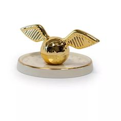 a golden apple with wings on top of a white plate next to a black and gold object