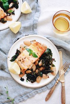 two plates with fish, beans and greens next to a glass of tea on a towel