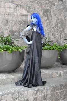 a woman with blue hair is dressed in a black dress and stands on some steps