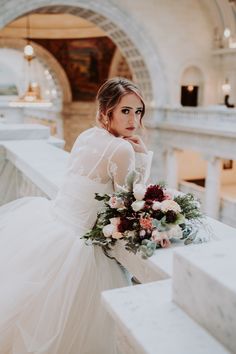 a woman in a wedding dress sitting on a ledge with her hand near her face