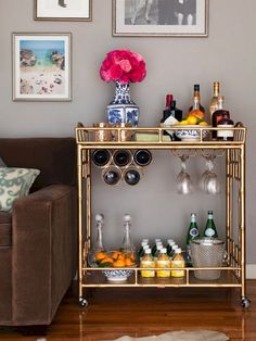 a gold bar cart with bottles and glasses on it next to a brown couch in a living room