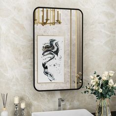 a bathroom sink sitting under a mirror next to a vase with white flowers in it